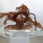 Copper wire artwork head and shoulder attached to perspex base placed on a white plinth in gallery space
